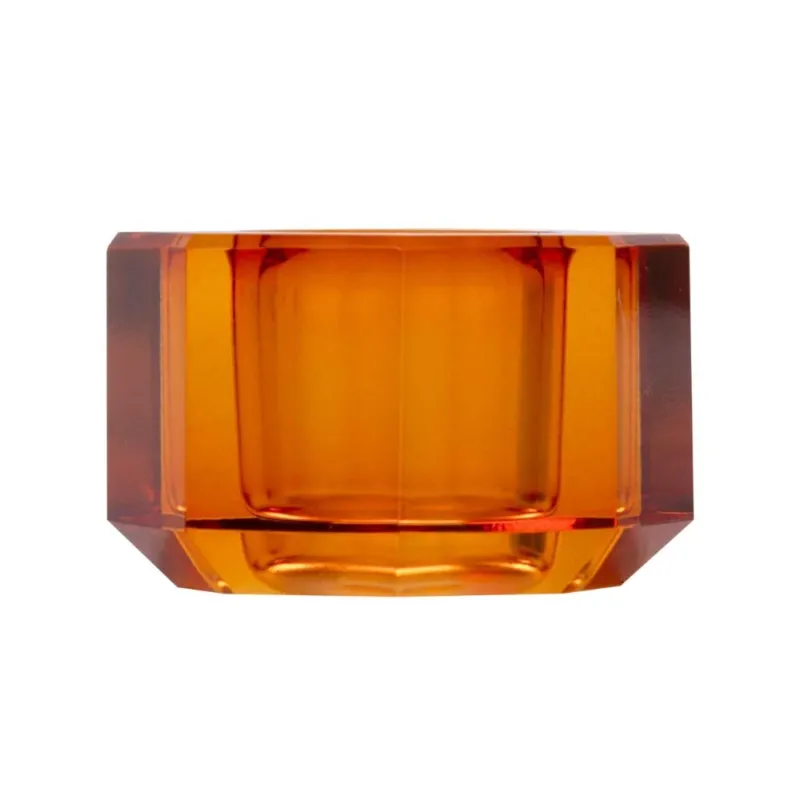 Ein kleiner Kerzenhalter aus Glas in Bernstein Kristall-Optik, bestehend aus mehreren geometrischen Flächen. Der Kerzenhalter hat eine moderne, facettierte Optik, die das Licht reflektiert